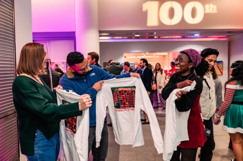 Guests at Montgomery Park 100th anniversary event hold up complimentary shirts and smile
