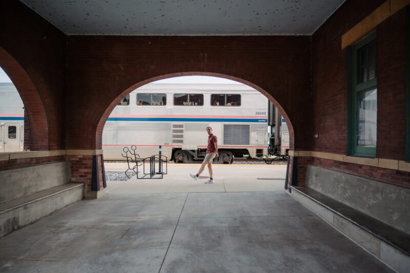 man walking past train under a brick arch