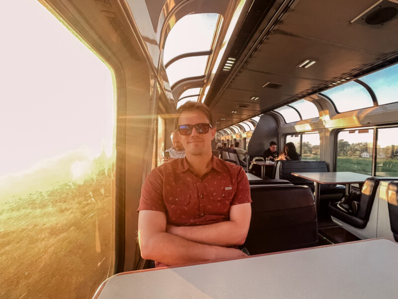 man in viewing car of train with sunrise behind him