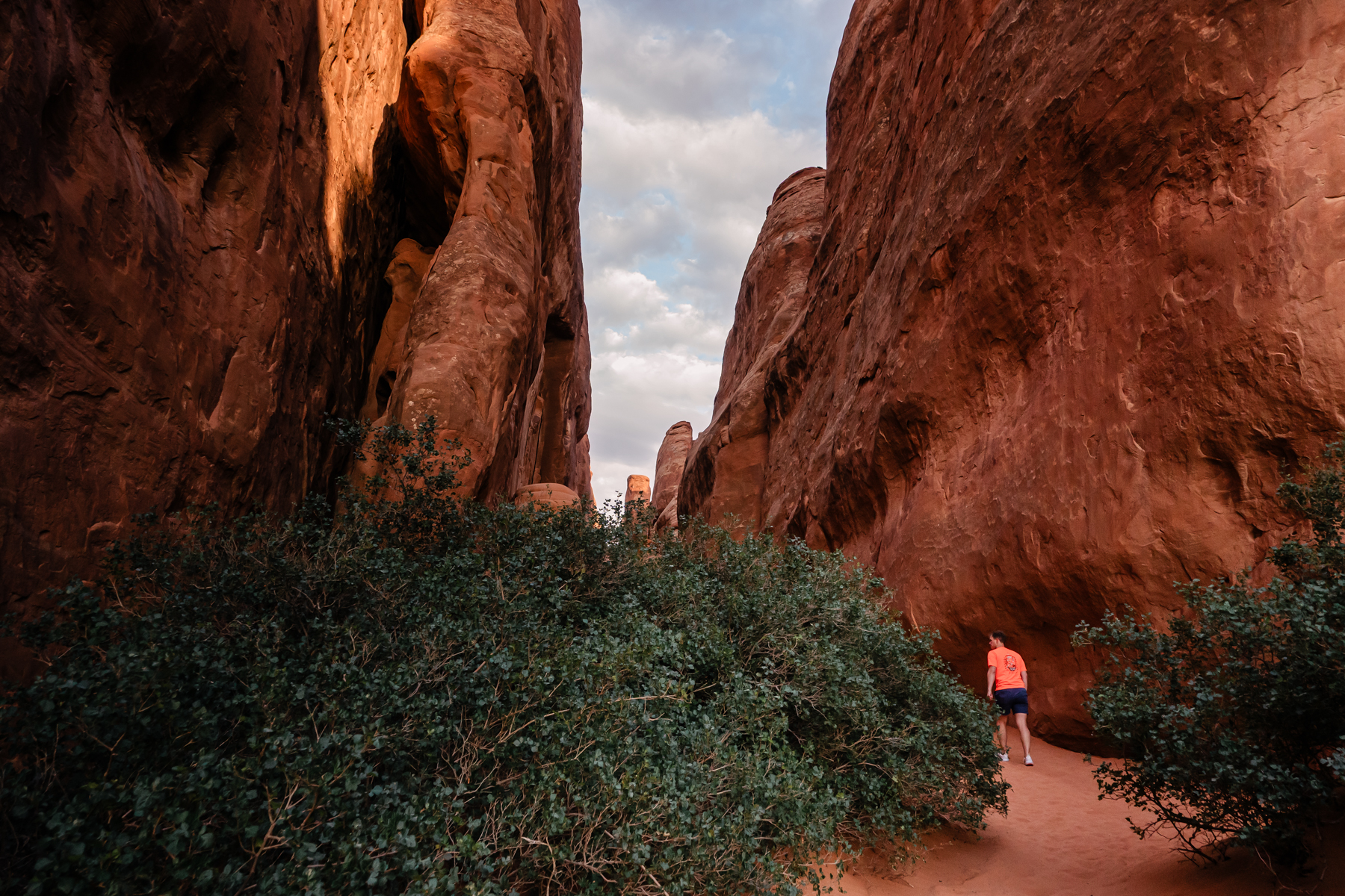 man walking between large rock structures at Arches National Park