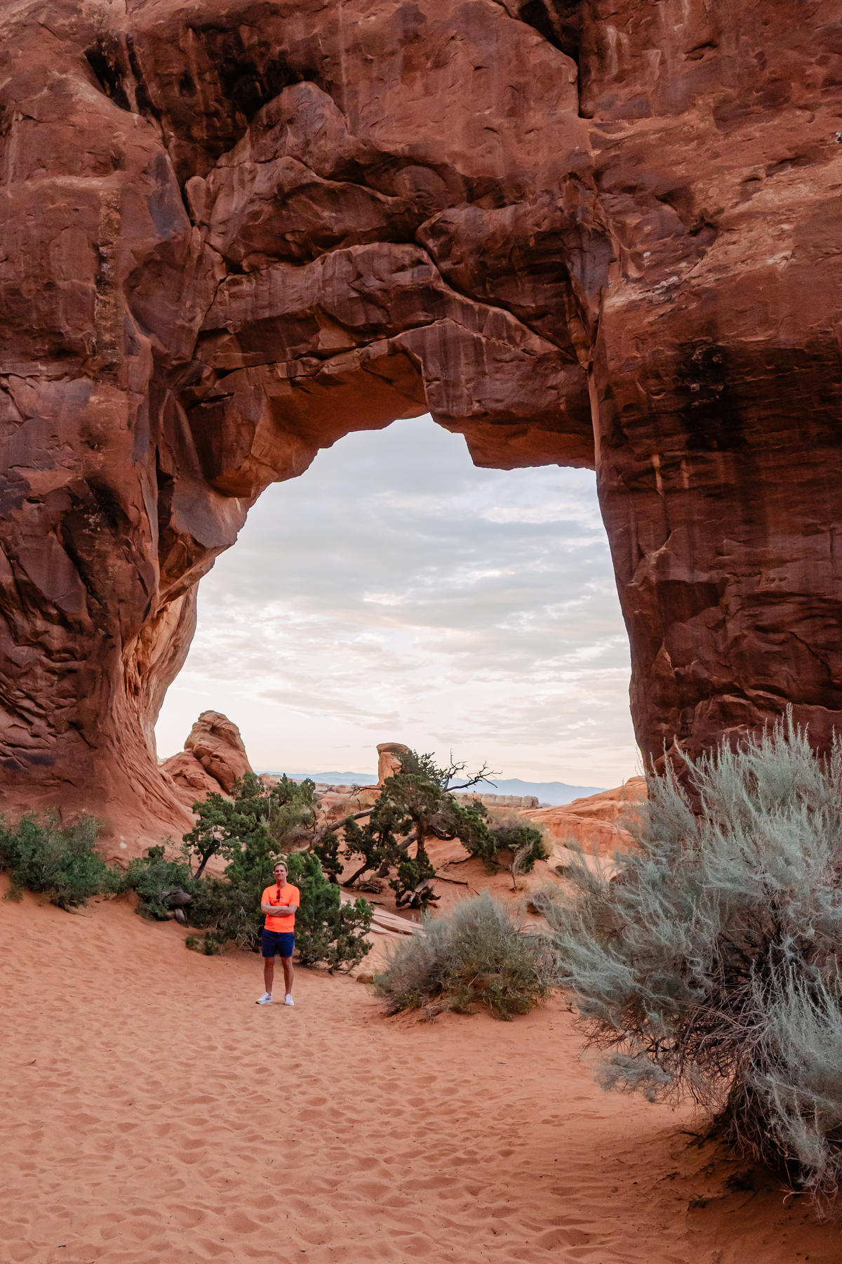 man posing in front of large arch rock