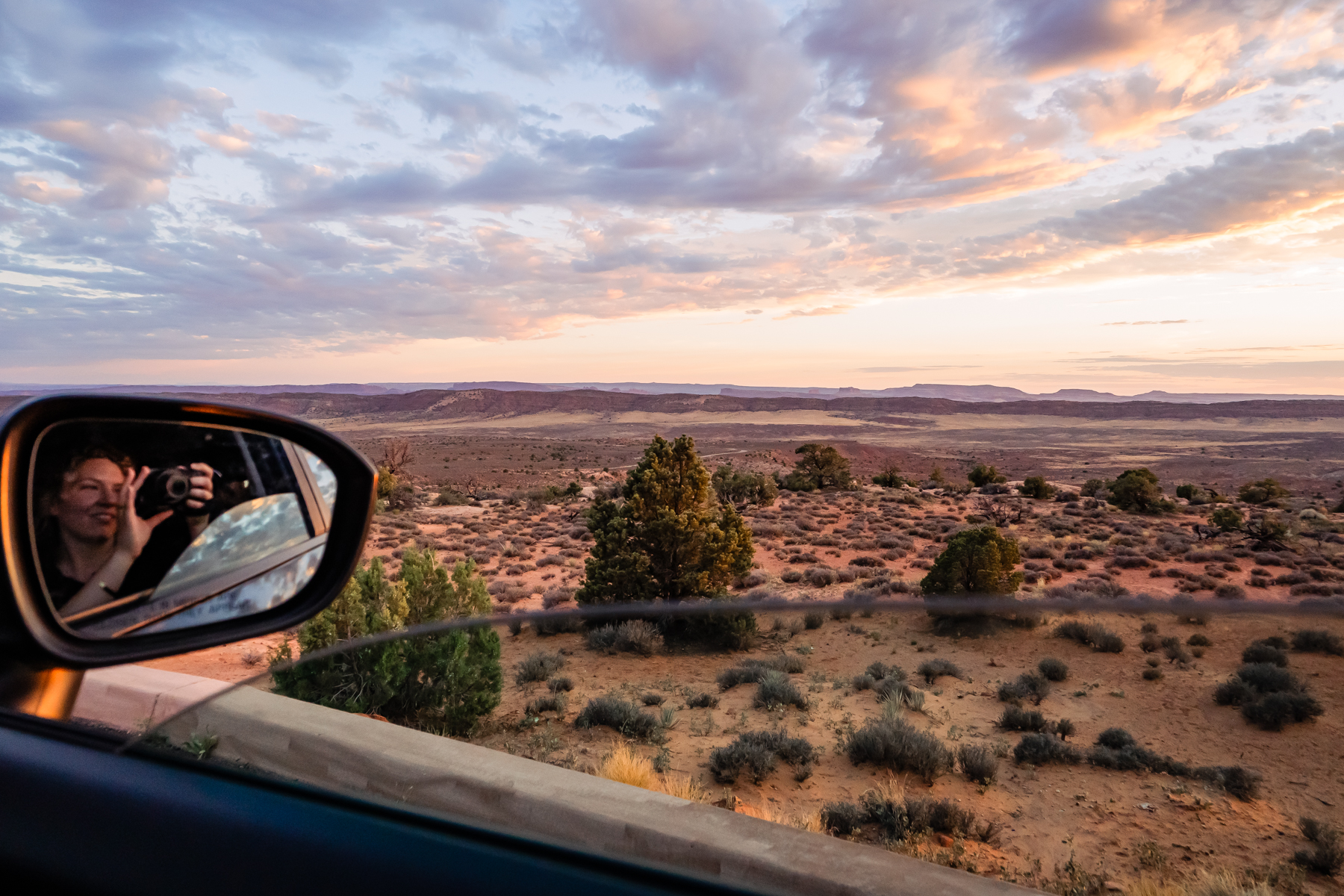 view of desert at sunset with photographer in side mirror