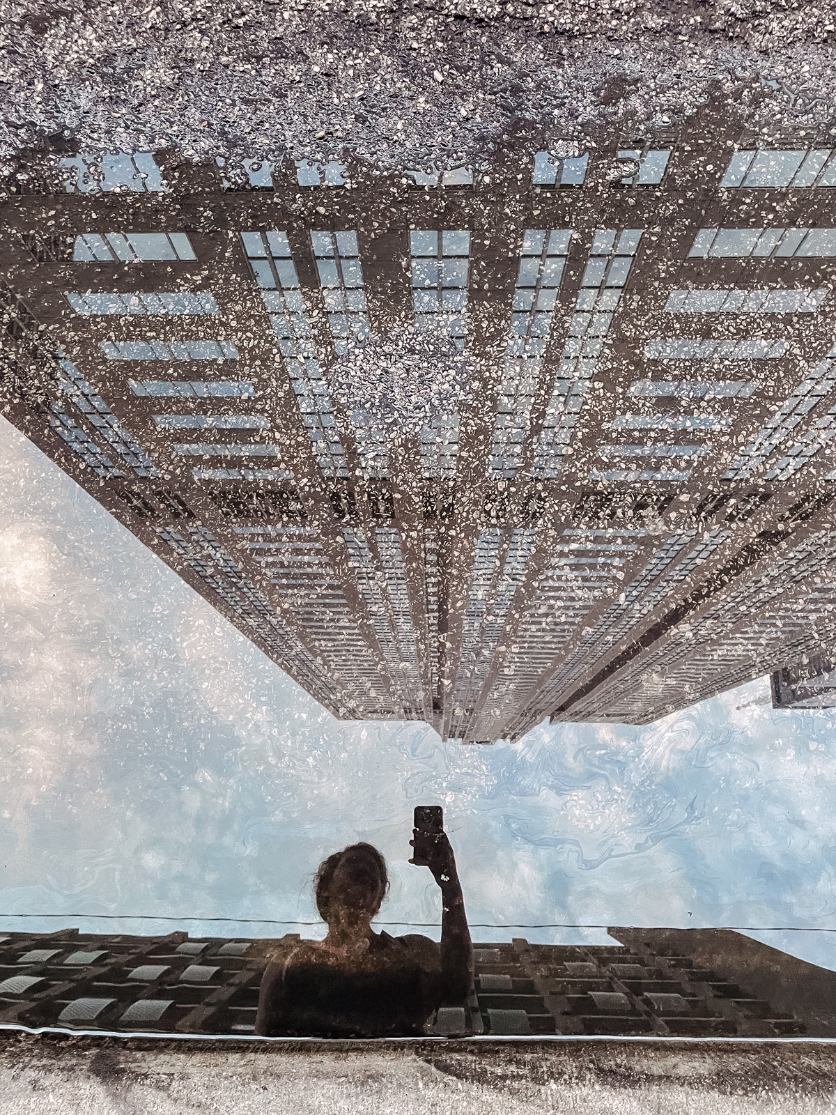 reflection of woman taking a photo on phone in a puddle on the road