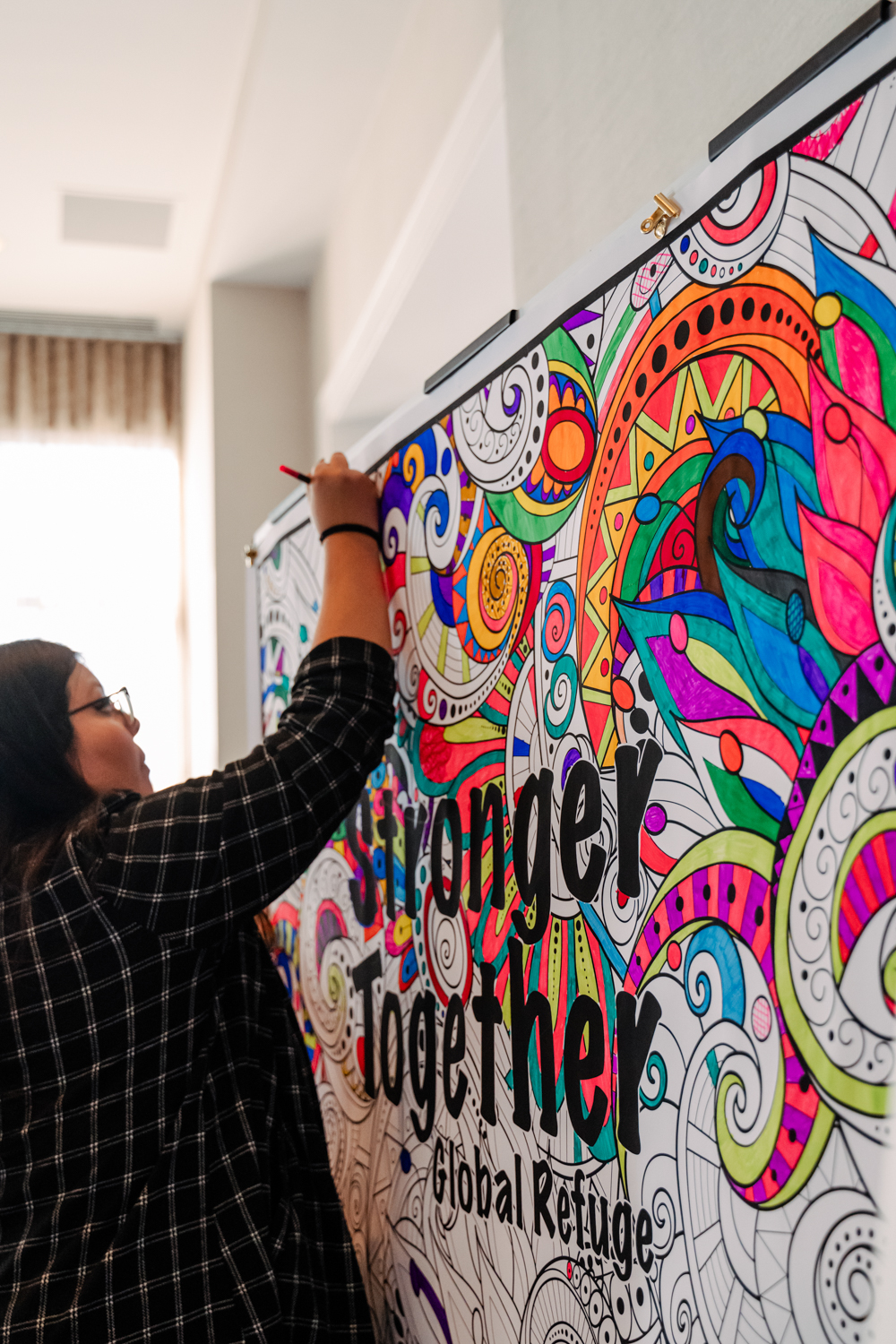 Global Refuge staff fills in a large poster with marker that reads "Stronger Together"
